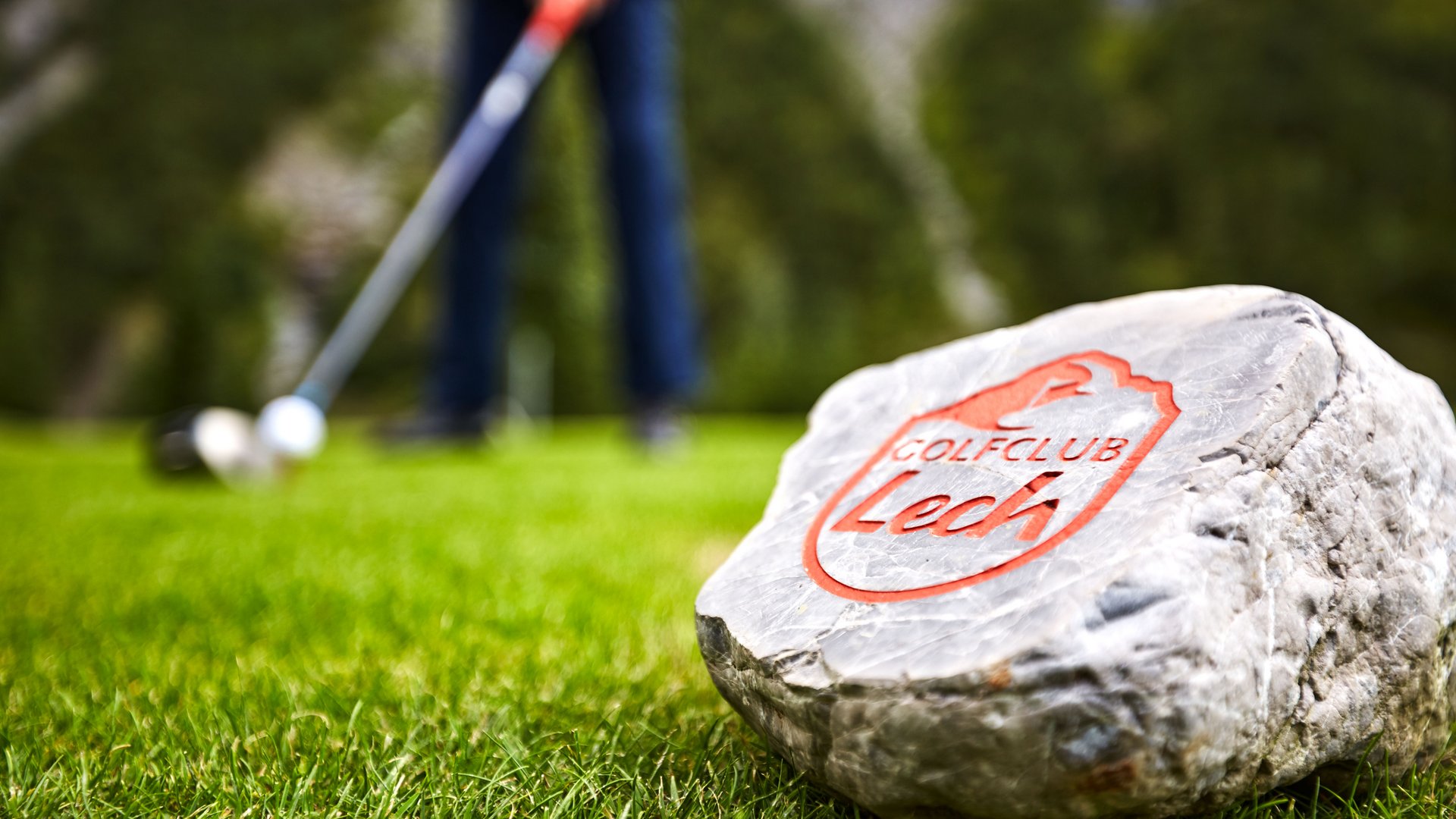 Membership im Golfclub Lech Stein mit Aufschrift Golfclub Lech auf dem Golfplatz mit unscharfem Golfer im Hintergrund