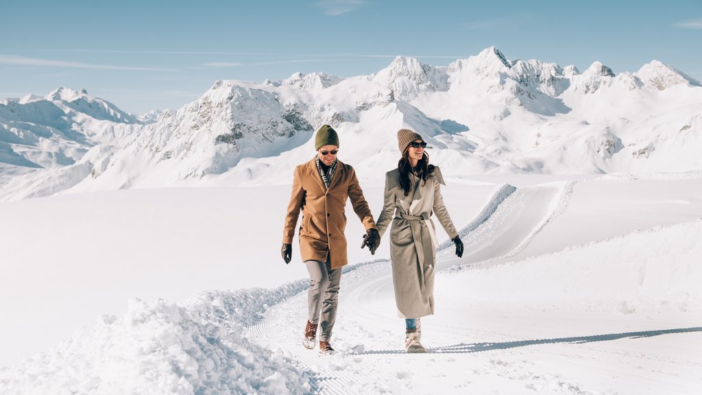 Unter 35 Paar hält Händchen und spaziert auf verschneiter Bergstraße bei Sonnenschein