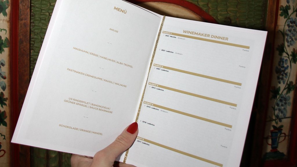 Hand holding menu with dishes and winemaker dinner wine list against decorative wood panel