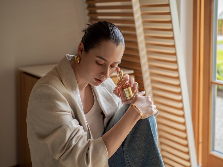 Woman holding and smelling perfume bottle in a neutral indoor setting