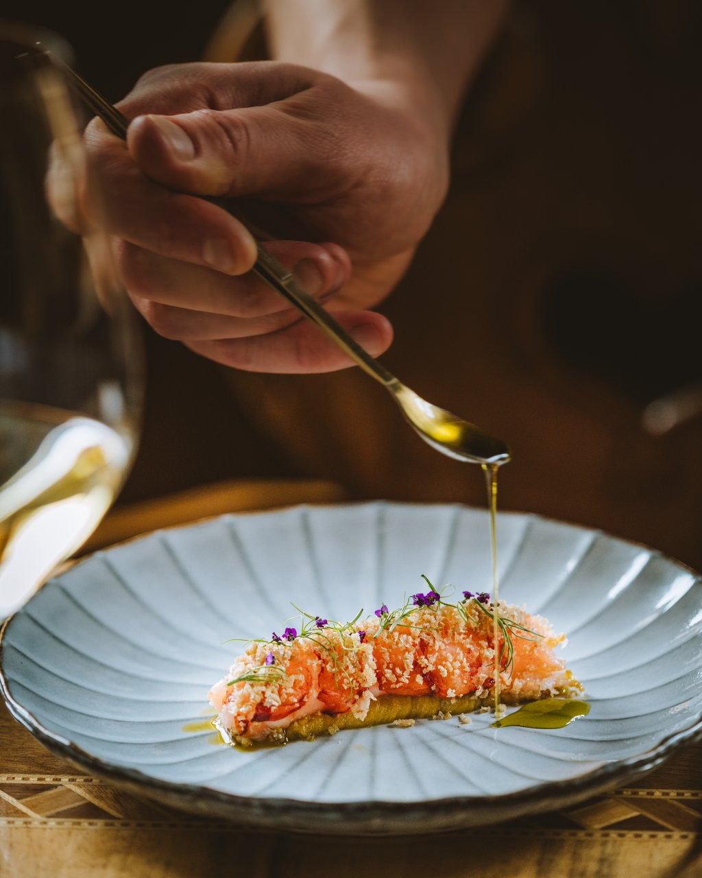 Hand drizzling oil over a plated dish with salmon and herbs