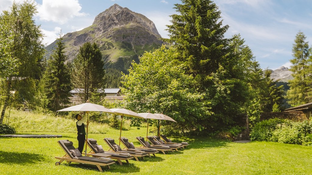 Pools & Garten im Hotel Post Lech am Arlberg | Wasser, Ruhe & alpine Natur Mann richtet Sonnenschirme bei Liegestühlen vor Bergkulisse in einem Garten auf