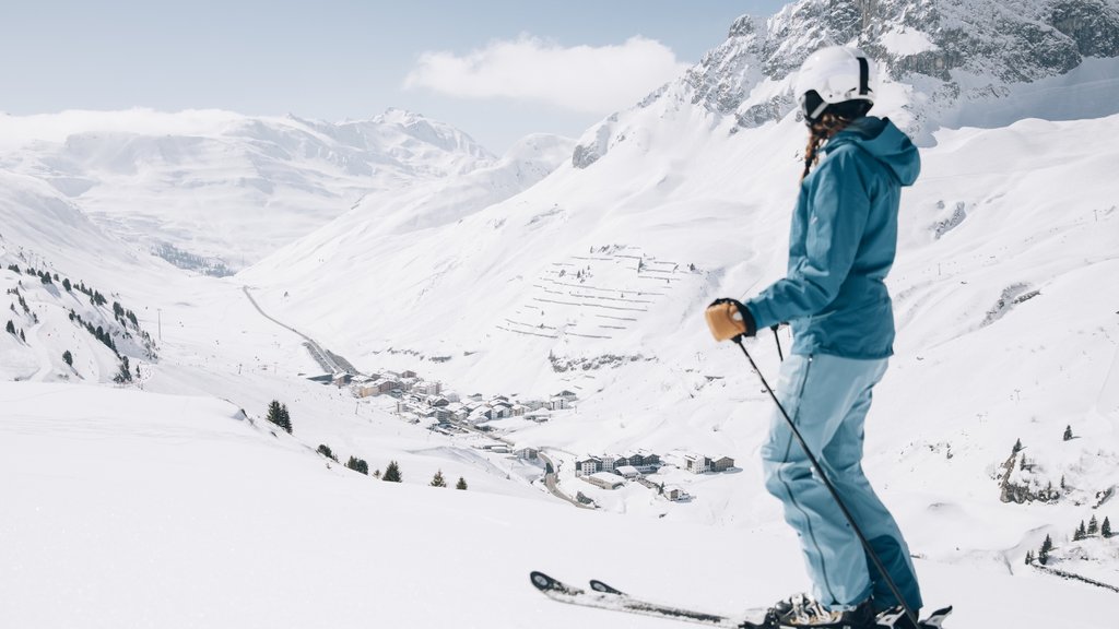 Frühlingsskilauf Skifahrerin in blauer Kleidung blickt auf verschneite Berge und Dorf im Tal