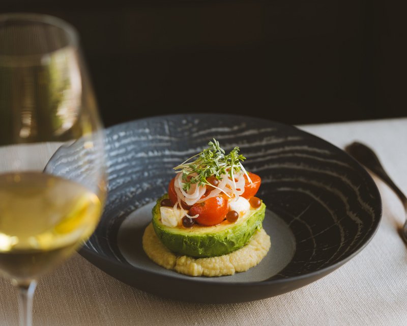 Avocadohälfte mit Kirschtomaten, Zwiebeln und Kresse auf cremigem Dip