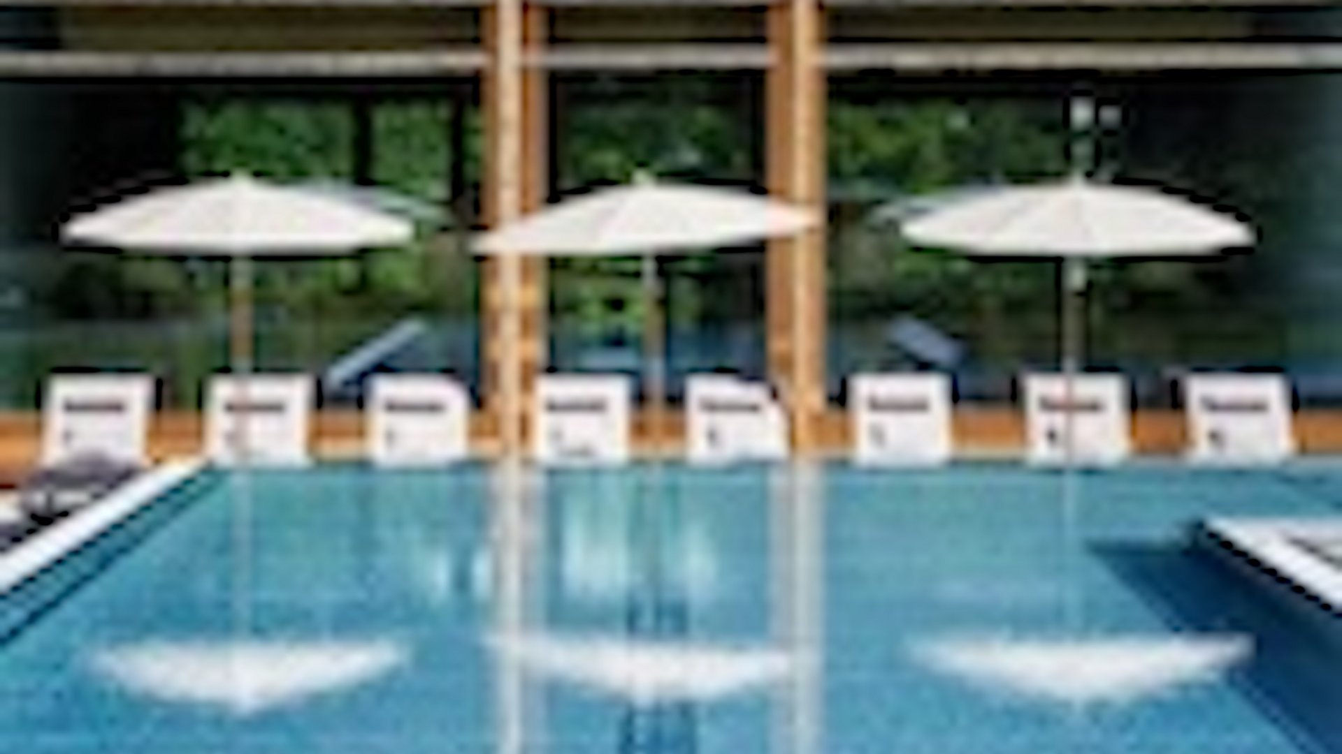 Spa Buchung im Hotel Post Lech Arlberg | Anwendungen & Termine reservieren Freizeitbereich mit Swimmingpool und Sonnenschirmen an einem modernen Gebäude