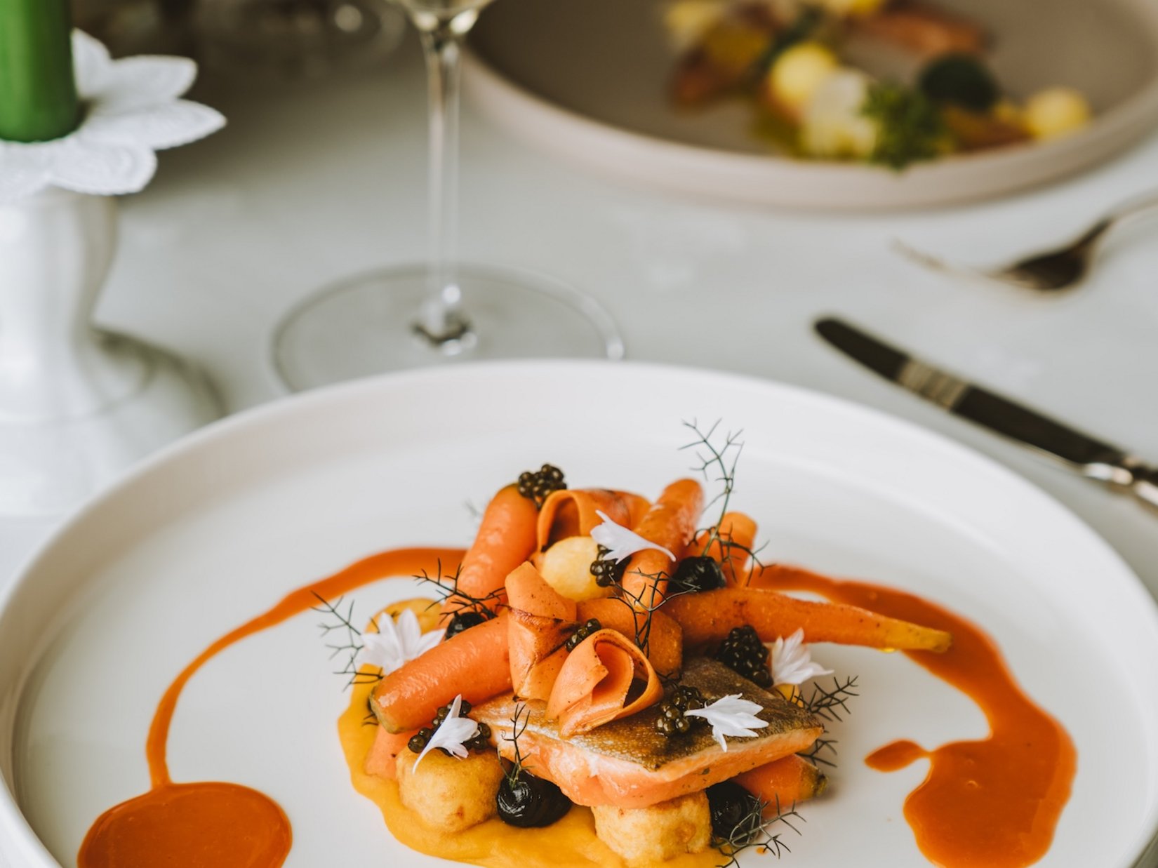 Gourmet dish with carrots and sauce on white plate, white wine in background
