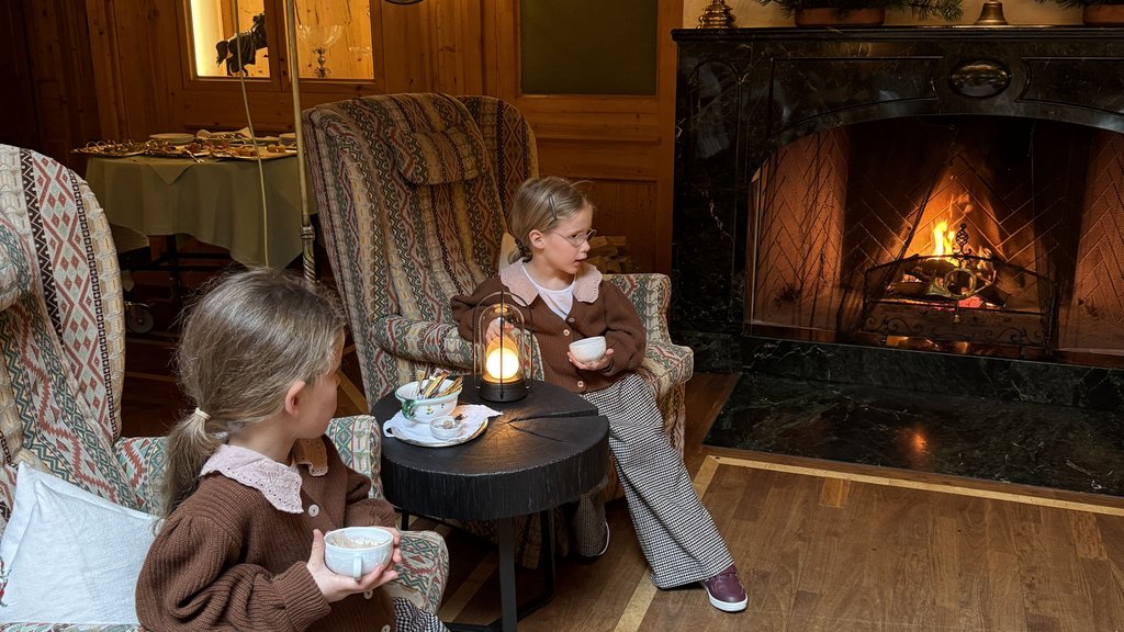 Zwei Mädchen sitzen mit Tee an einem Kamin in einem gemütlichen Holzraum
