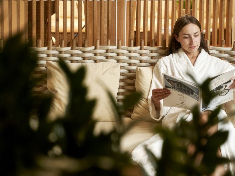 Woman in bathrobe reading a magazine while sitting on a wooden bench