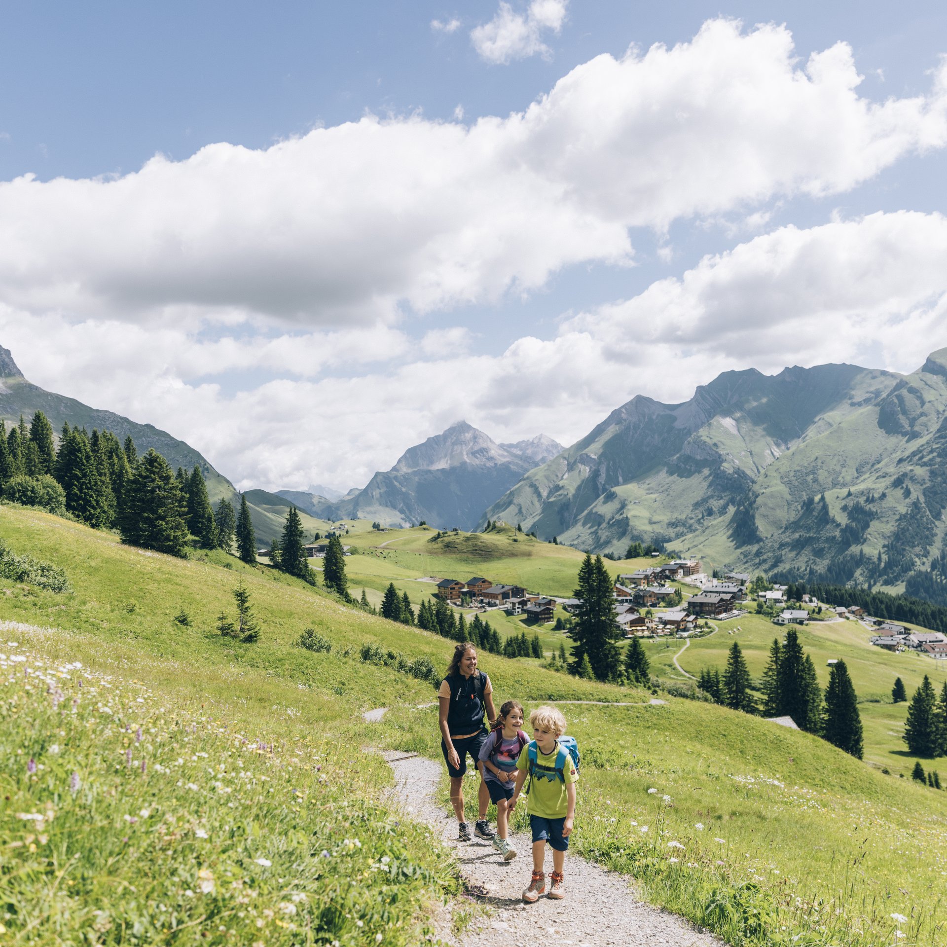 Familie wandert auf einem Bergweg mit Alpenlandschaft und blauem Himmel