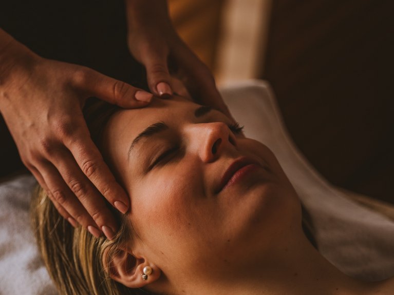 Frau erhält entspannende Gesichtsmassage bei gedämpftem Licht