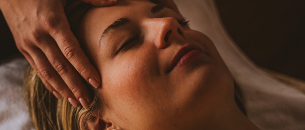 Frau erhält entspannende Gesichtsmassage bei gedämpftem Licht