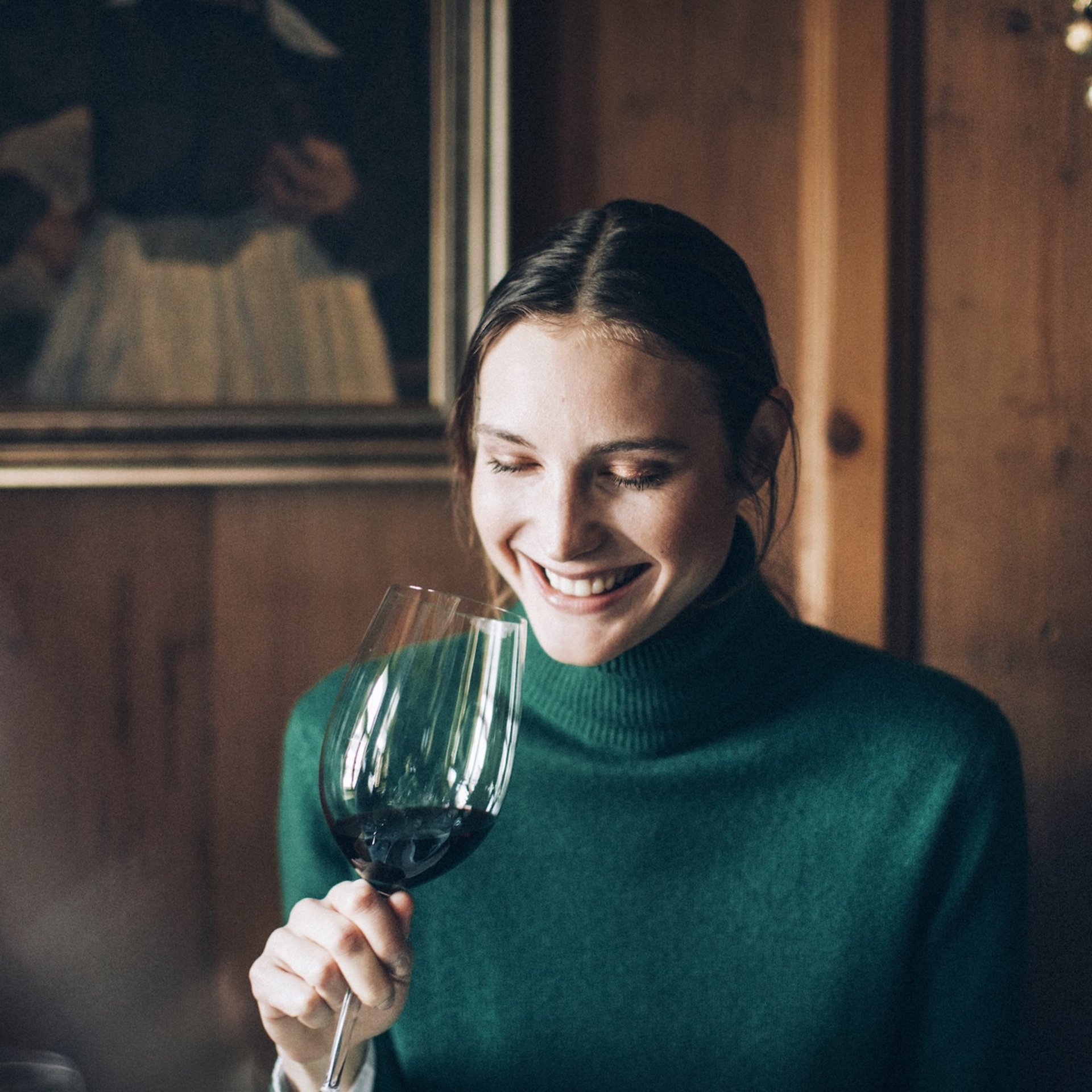 Frau in grünem Pullover lächelt und hält ein Glas Rotwein