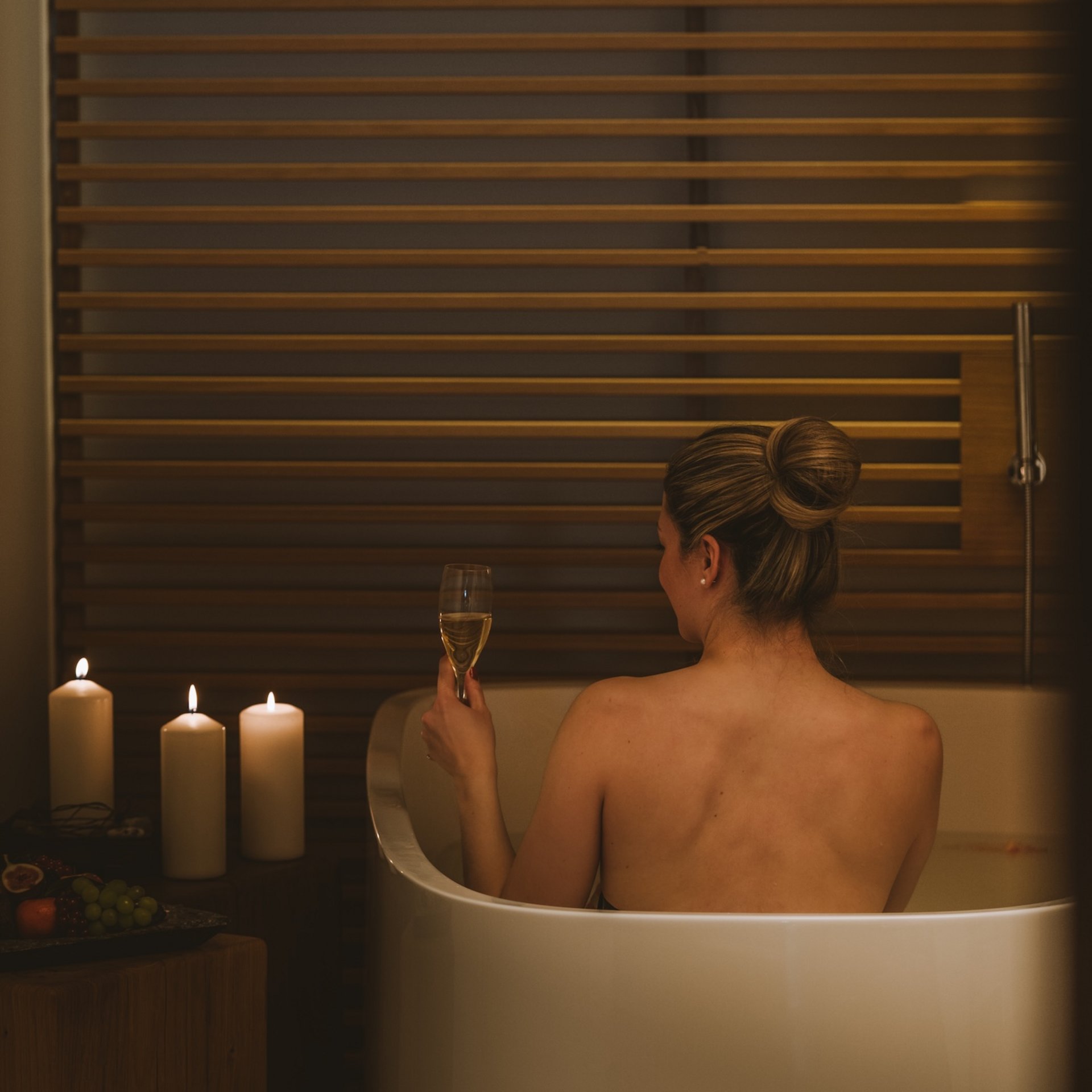 Frau entspannt in der Badewanne mit Kerzen und einem Glas Wein