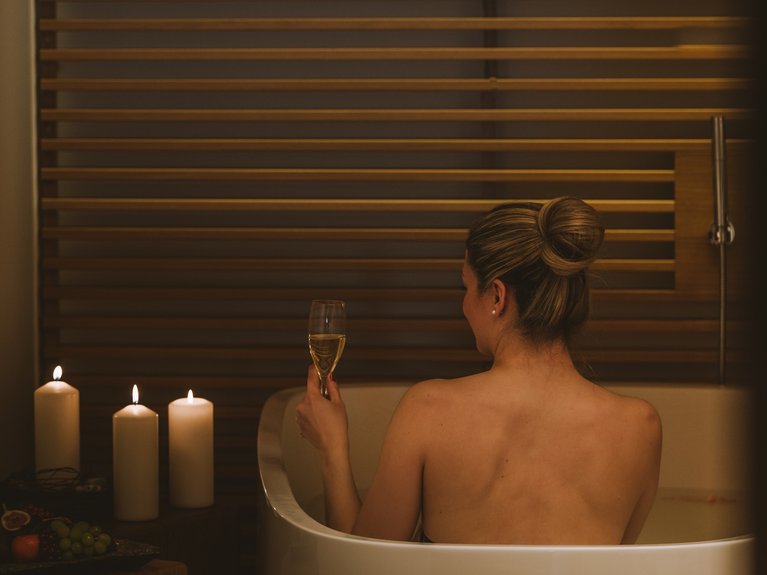 Frau entspannt in der Badewanne mit Kerzen und einem Glas Wein