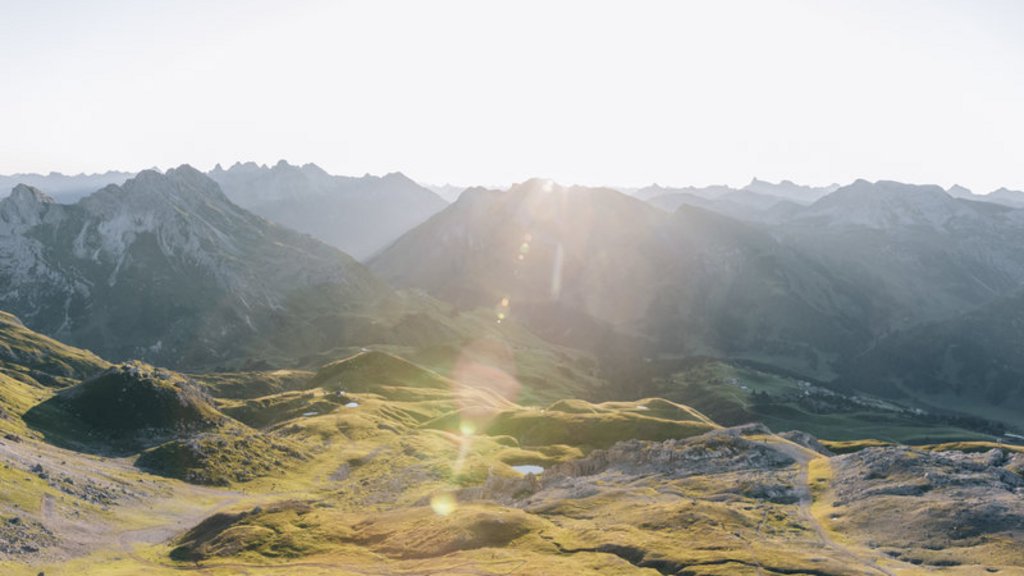 Sonnenaufgang über grasbewachsenen Bergen mit steilen Gipfeln im Hintergrund