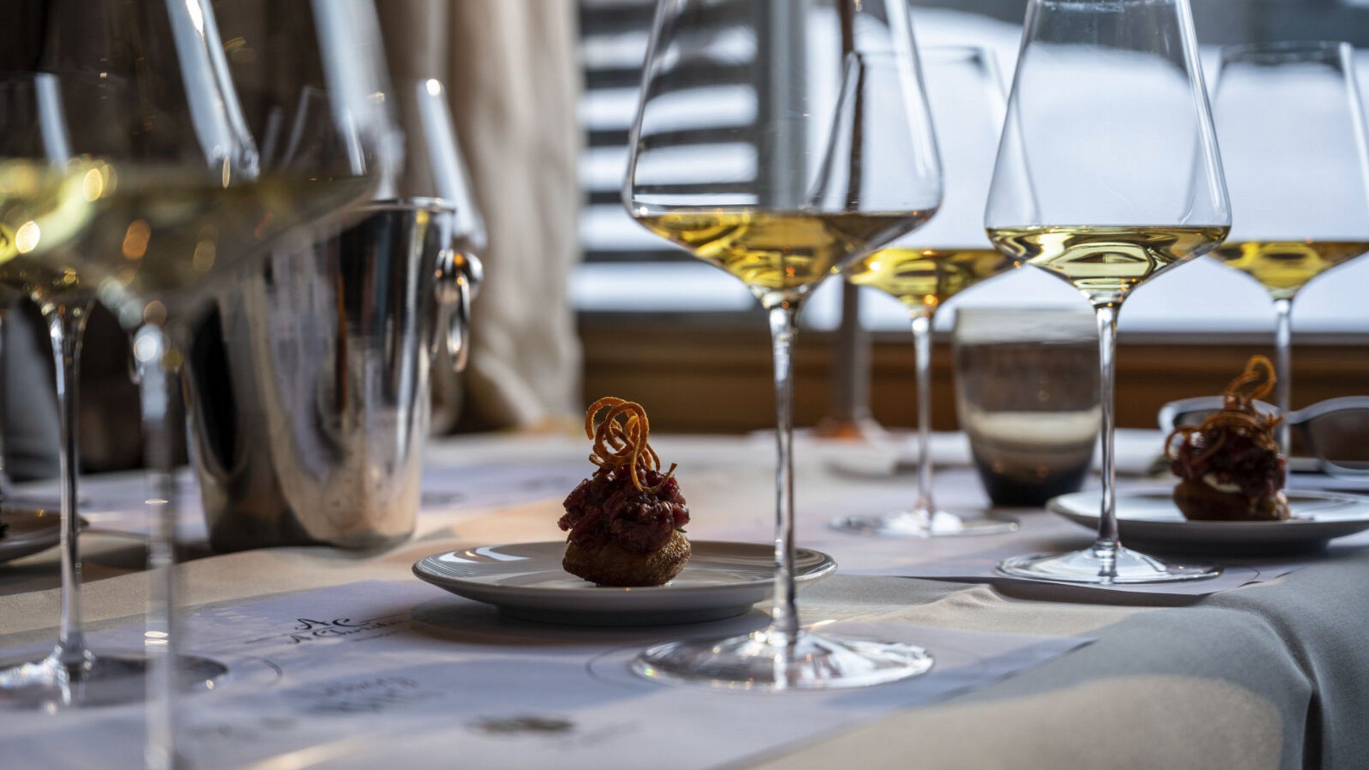 Wenn große Weine auf alpine Gastfreundschaft treffen Weingläser mit Weißwein und kleine Häppchen auf einem gedeckten Tisch