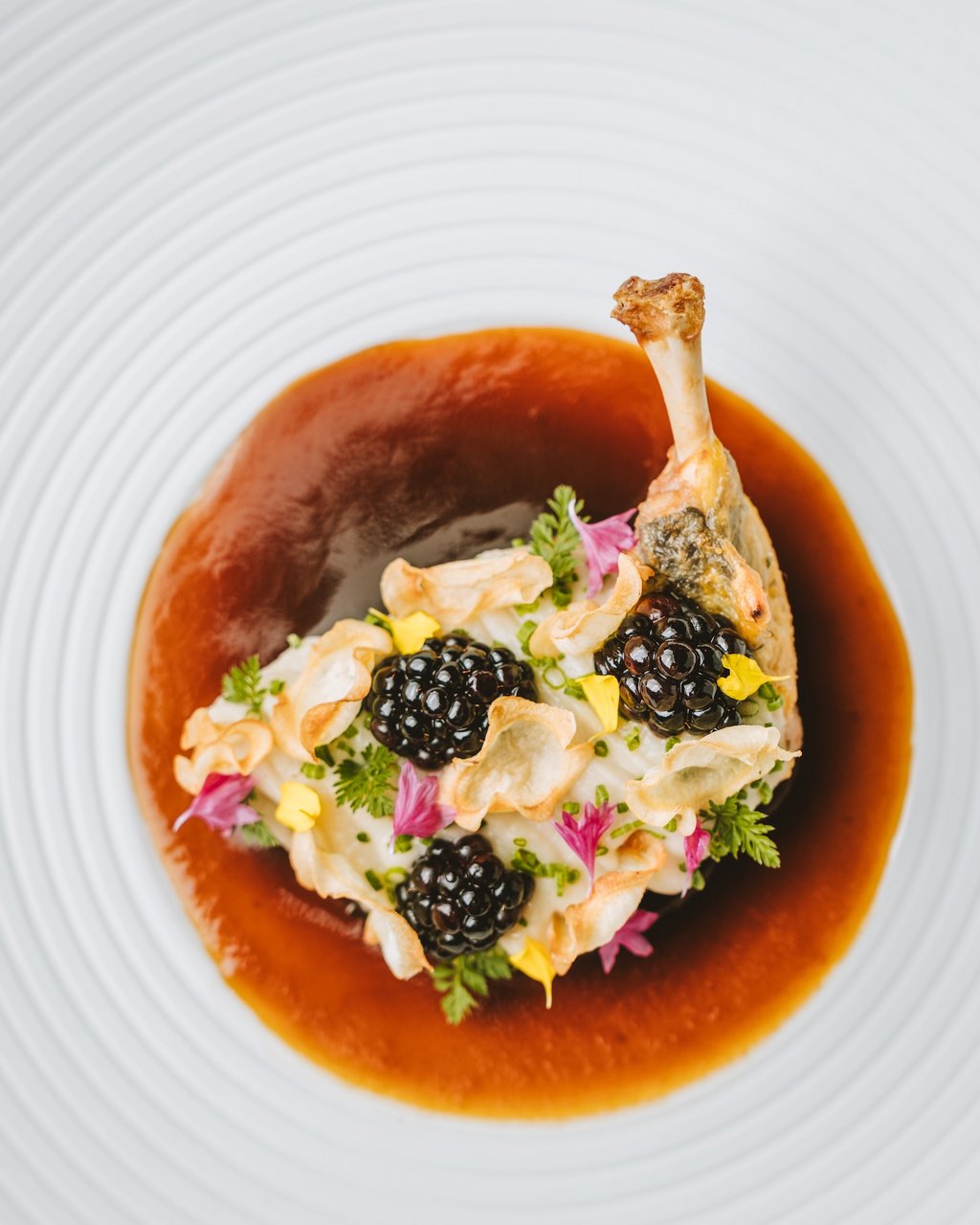 Gourmet-Geflügelgericht mit Sauce und essbaren Blumen auf weißem Teller