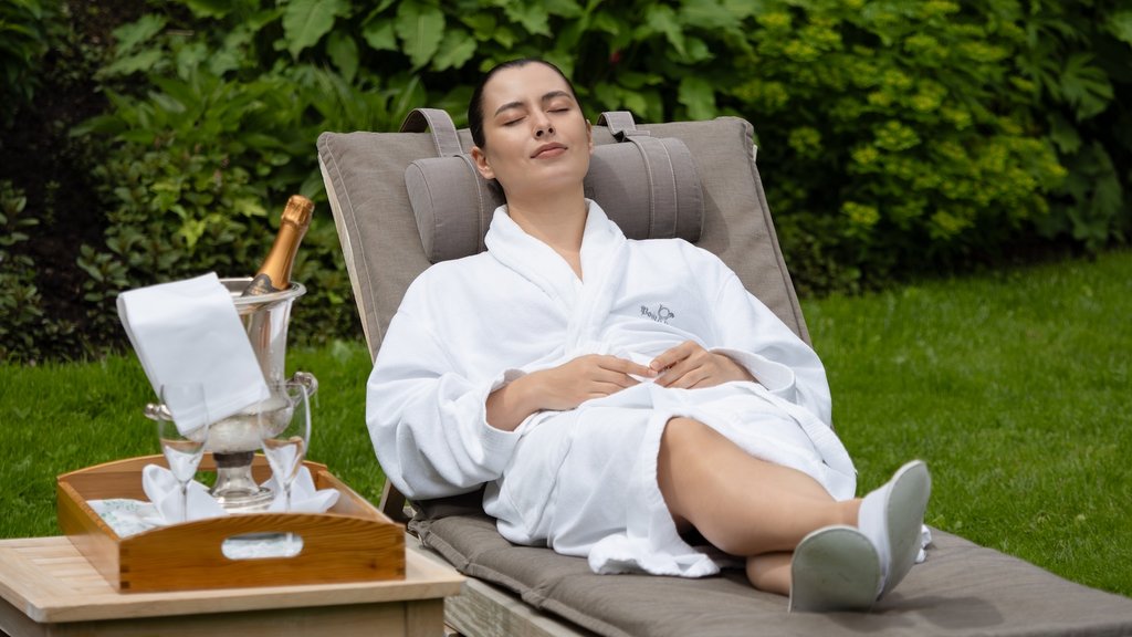 Woman relaxing on lounge chair in robe with champagne and glasses in garden