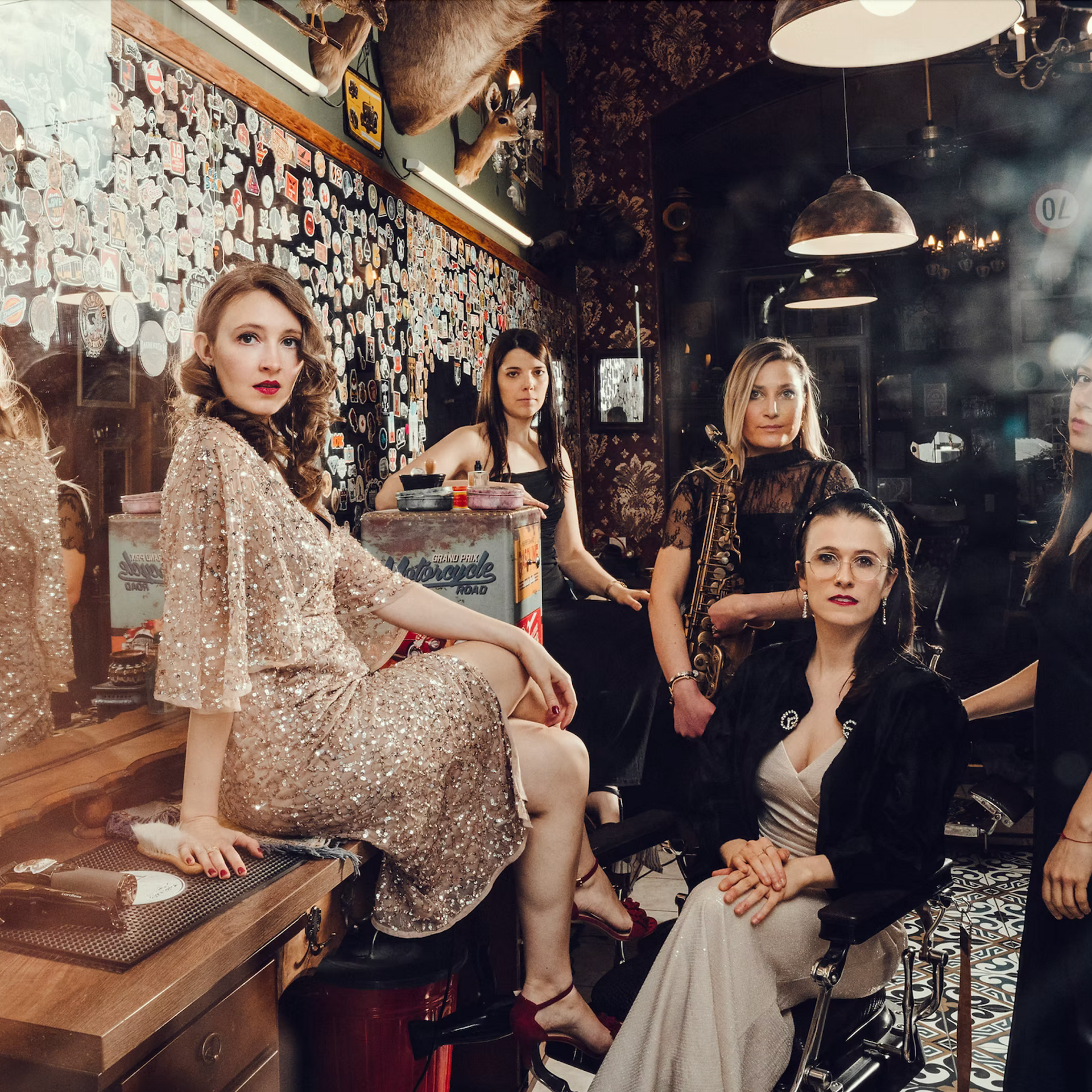 Fünf elegant gekleidete Frauen posieren in einem Retro-Barbershop mit Spiegel und Dekor