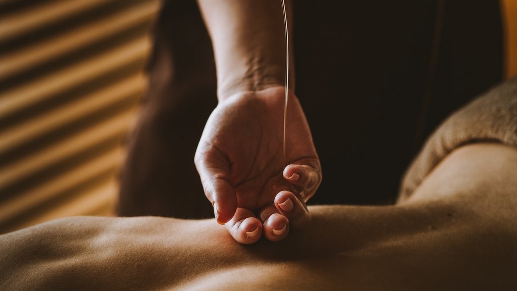 Anwendungen in der Post Hand gießt Massageöl auf den Rücken während einer Ölmassage