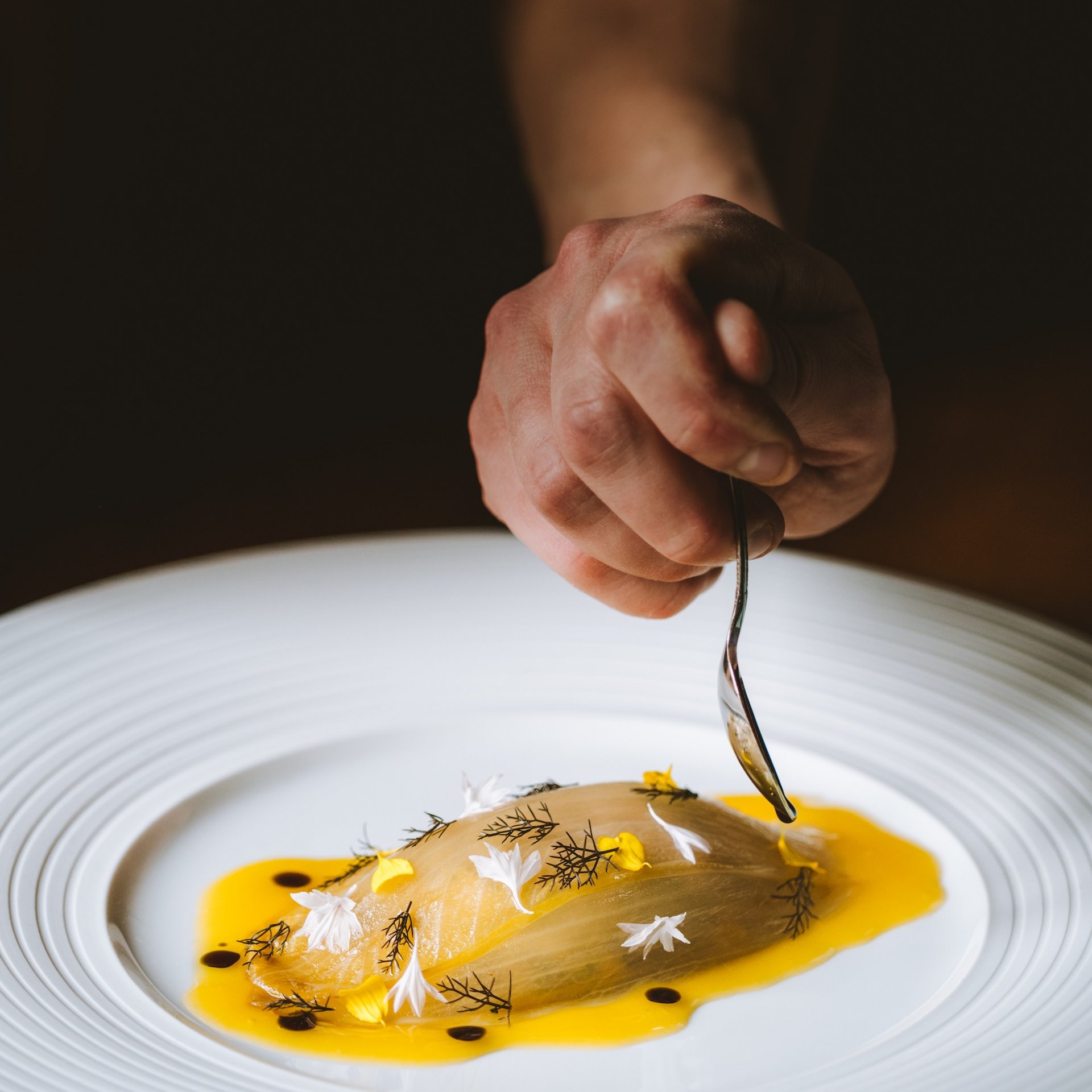 Indulge at Hotel Post Lech at the Arlberg | Alpine Luxury & Culinary Excellence Hand holding spoon over fine dish with sauce and edible flowers