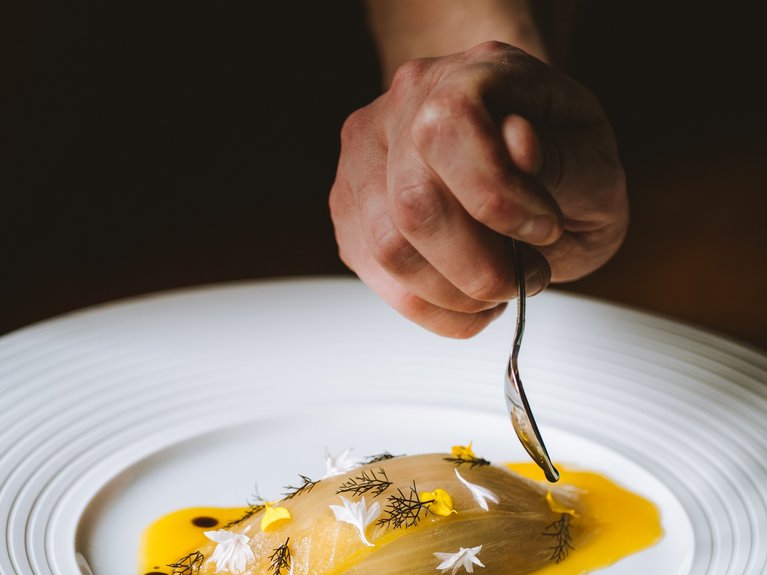 Hand mit Löffel, serviert feines Gericht mit Sauce und essbaren Blüten