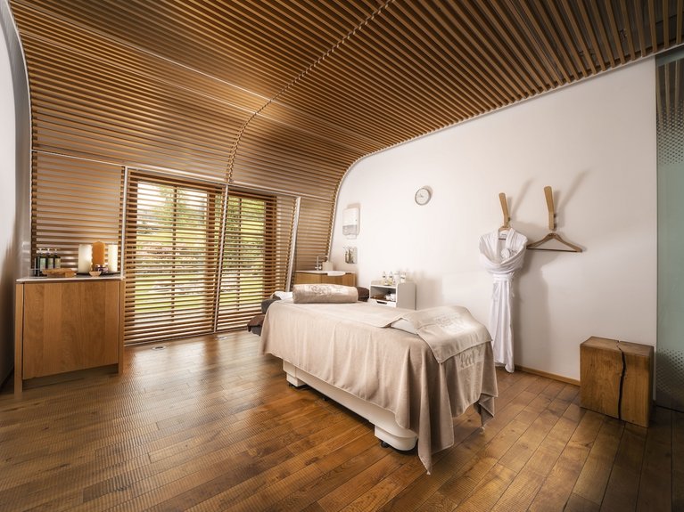 Treatment room with massage table and wooden slatted ceiling in warm light