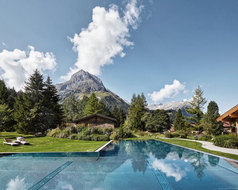 Schwimmbad vor Bergen und Bäumen unter blauem Himmel mit Wolken
