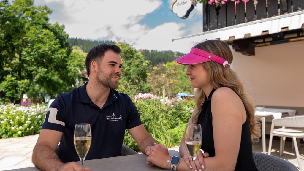 Paar hält Händchen und trinkt Sekt in einem Außenbereich bei sonnigem Wetter