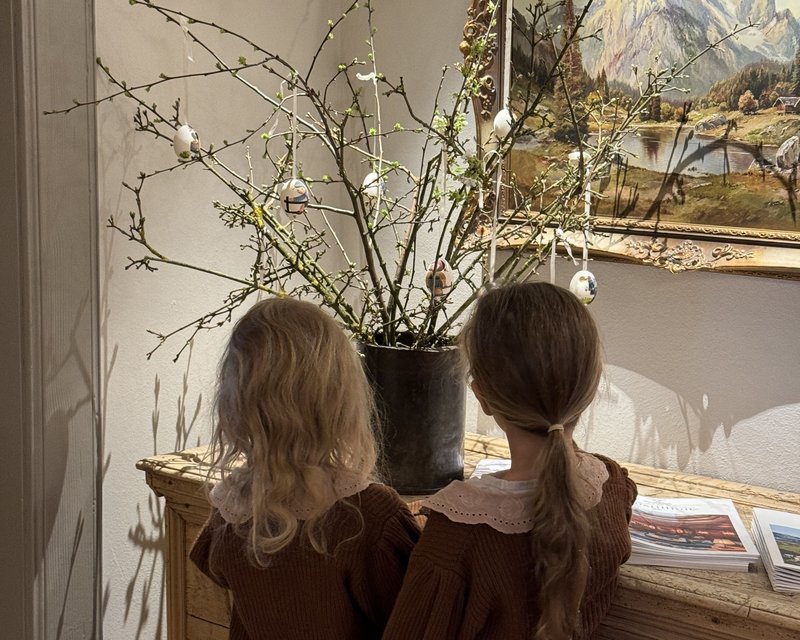 Zwei Kinder schauen auf einen Holztisch mit blühenden Ästen und bemalten Ostereiern