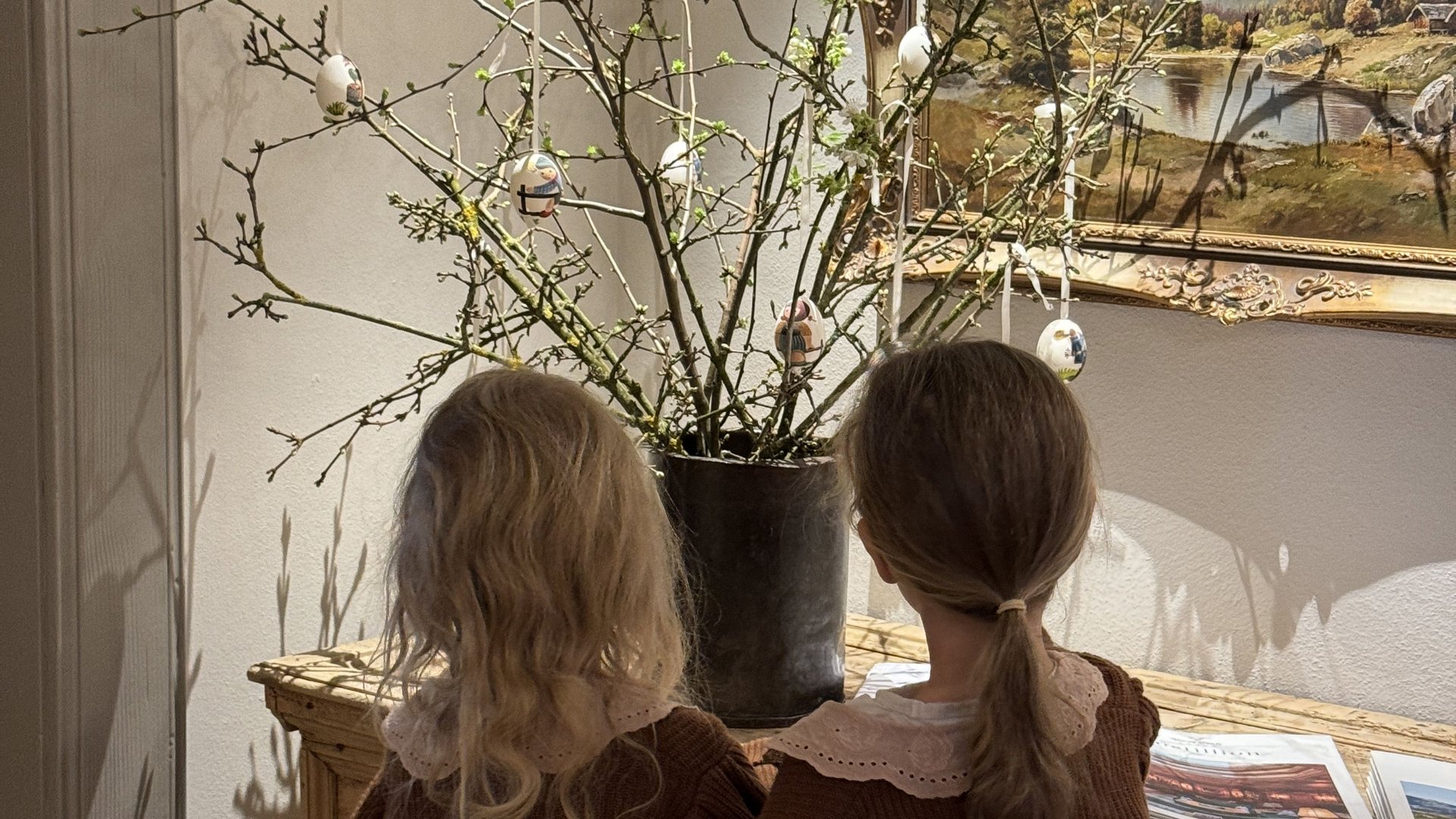 Zwei Kinder schauen auf einen Holztisch mit blühenden Ästen und bemalten Ostereiern