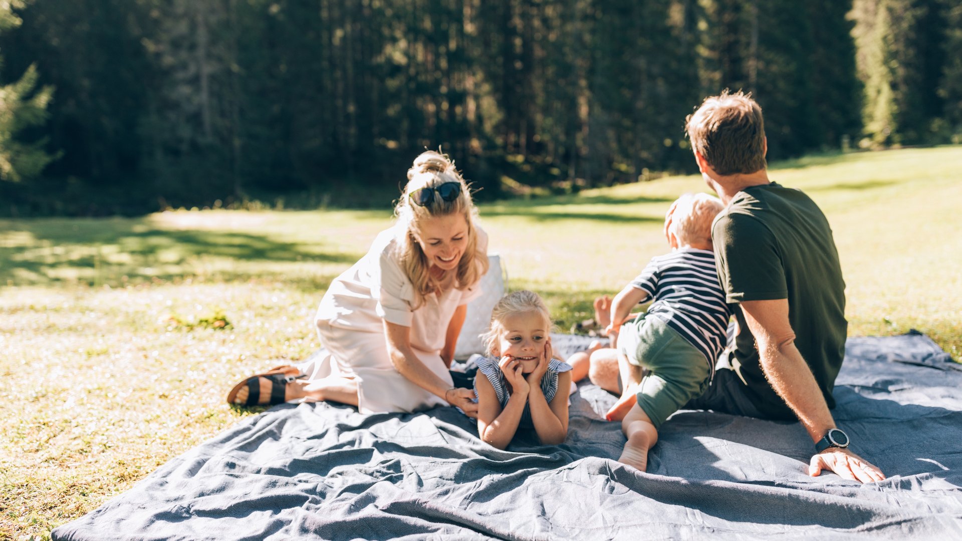Wenn gemeinsame Zeit zum größten Luxus wird Familie mit zwei Kindern entspannt auf einer Decke im sonnigen Park