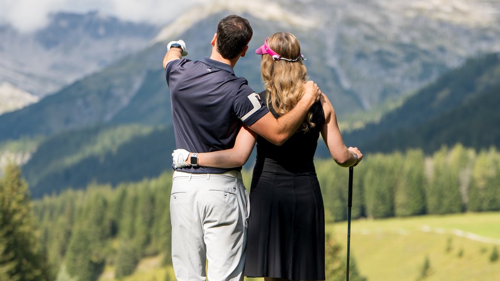 Paar auf Golfplatz umarmt sich und blickt auf Berge und Landschaft
