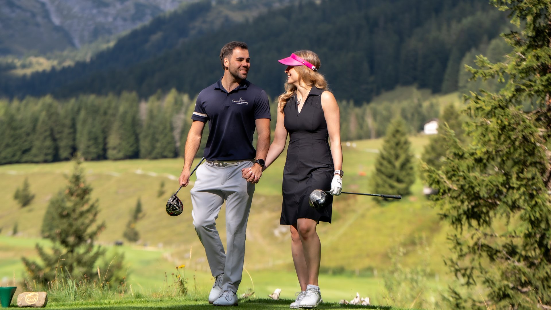 Paar beim Golfspielen in den Bergen hält Händchen und lächelt sich an