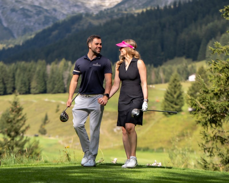 Paar beim Golfspielen in den Bergen hält Händchen und lächelt sich an