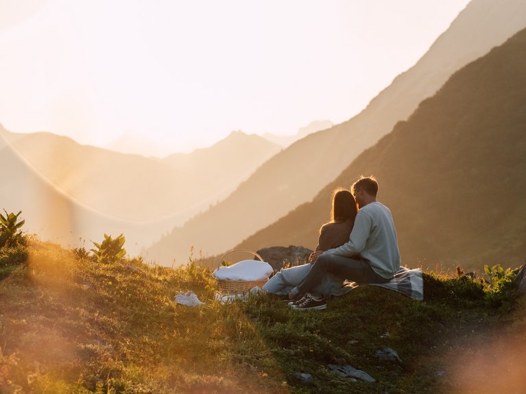 Couple sitting on picnic blanket in mountains at sunset