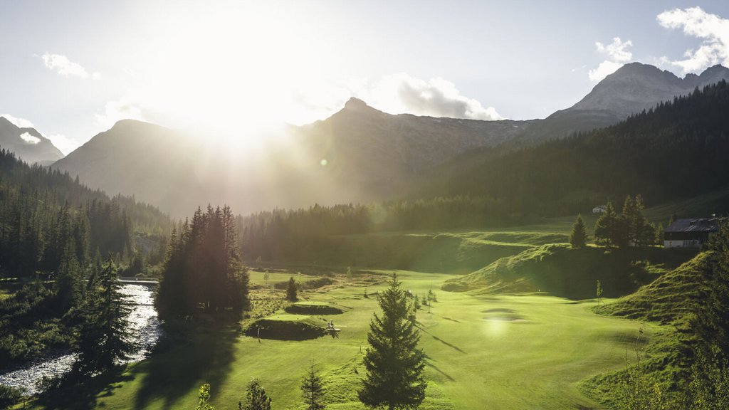 Sonnenuntergang über grünem Tal mit Fluss, Bäumen und Bergen im Hintergrund