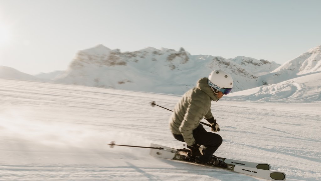 Skifahrer in Schutzhelm fährt auf einer verschneiten Piste in den Bergen