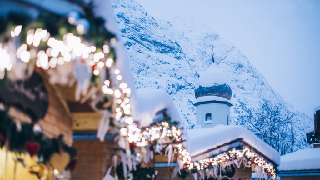 Adventzauber Verschneite Weihnachtsmarktstände mit Lichterketten vor Bergkulisse und Kirchturm