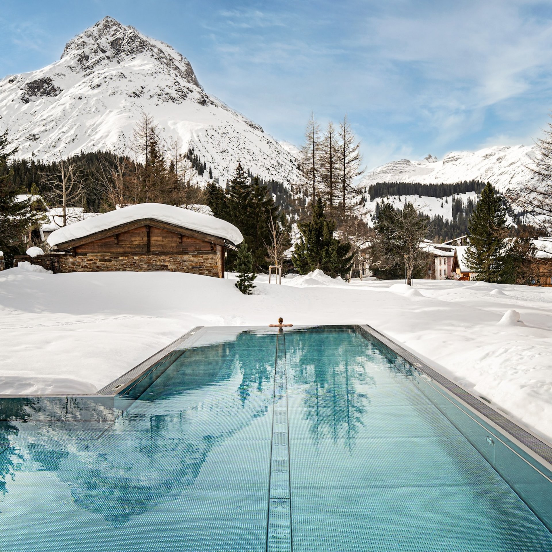 Winterurlaub in Lech am Arlberg | Skifahren, Genuss & Erholung im Hotel Post Lech Beheizter Außenpool vor verschneitem Berg und alpiner Landschaft
