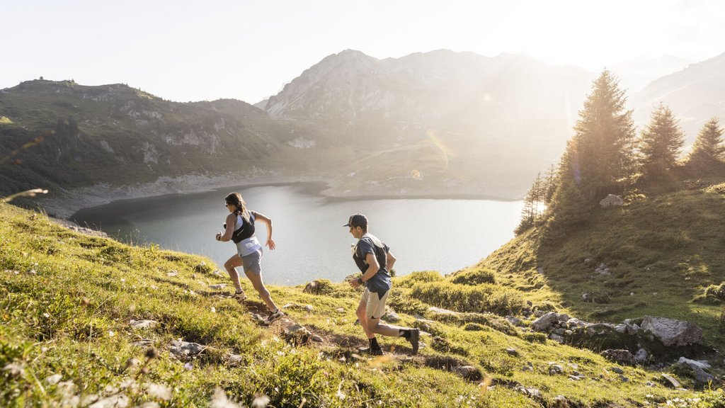Wenn Ruhe zum Luxus wird Zwei Personen laufen auf einem Bergpfad mit See und Bergen im Hintergrund