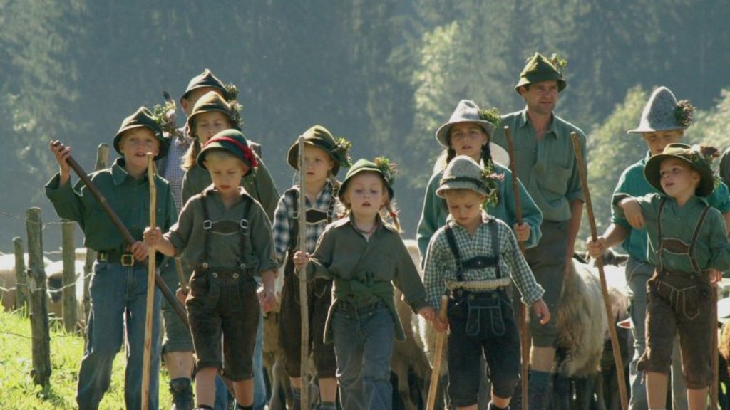 Children and an adult in traditional clothing herding sheep on a country road with forest background