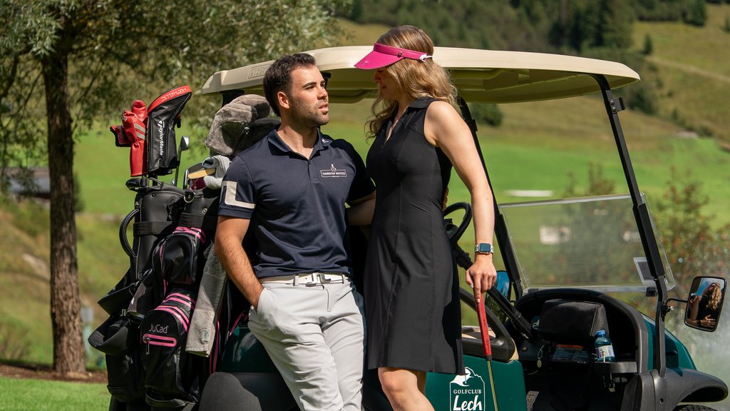 Paar lehnt an Golfcart auf Golfplatz umgeben von Bäumen und Grünfläche