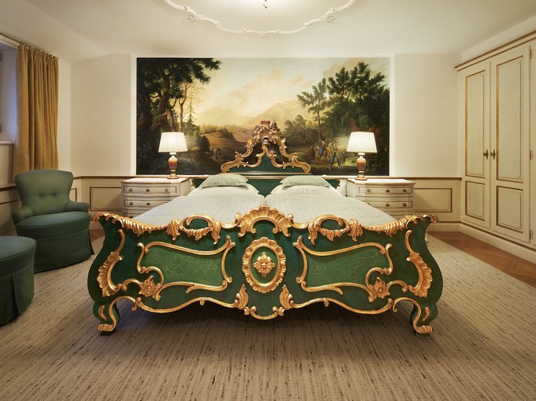 Antique bedroom with green and gold bed and landscape painting on the wall