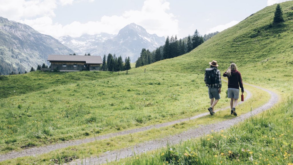 Zwei Wanderer auf Wanderweg in Alpenlandschaft mit Hütte und Berg