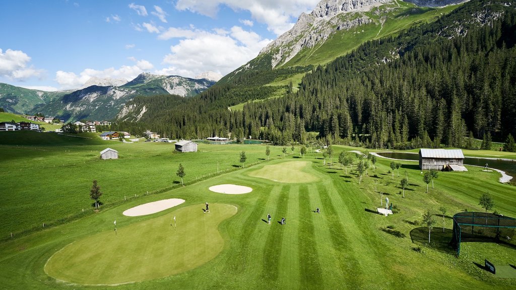 Golfspieler auf grünem Golfplatz vor Alpenlandschaft mit Bergen und Wäldern