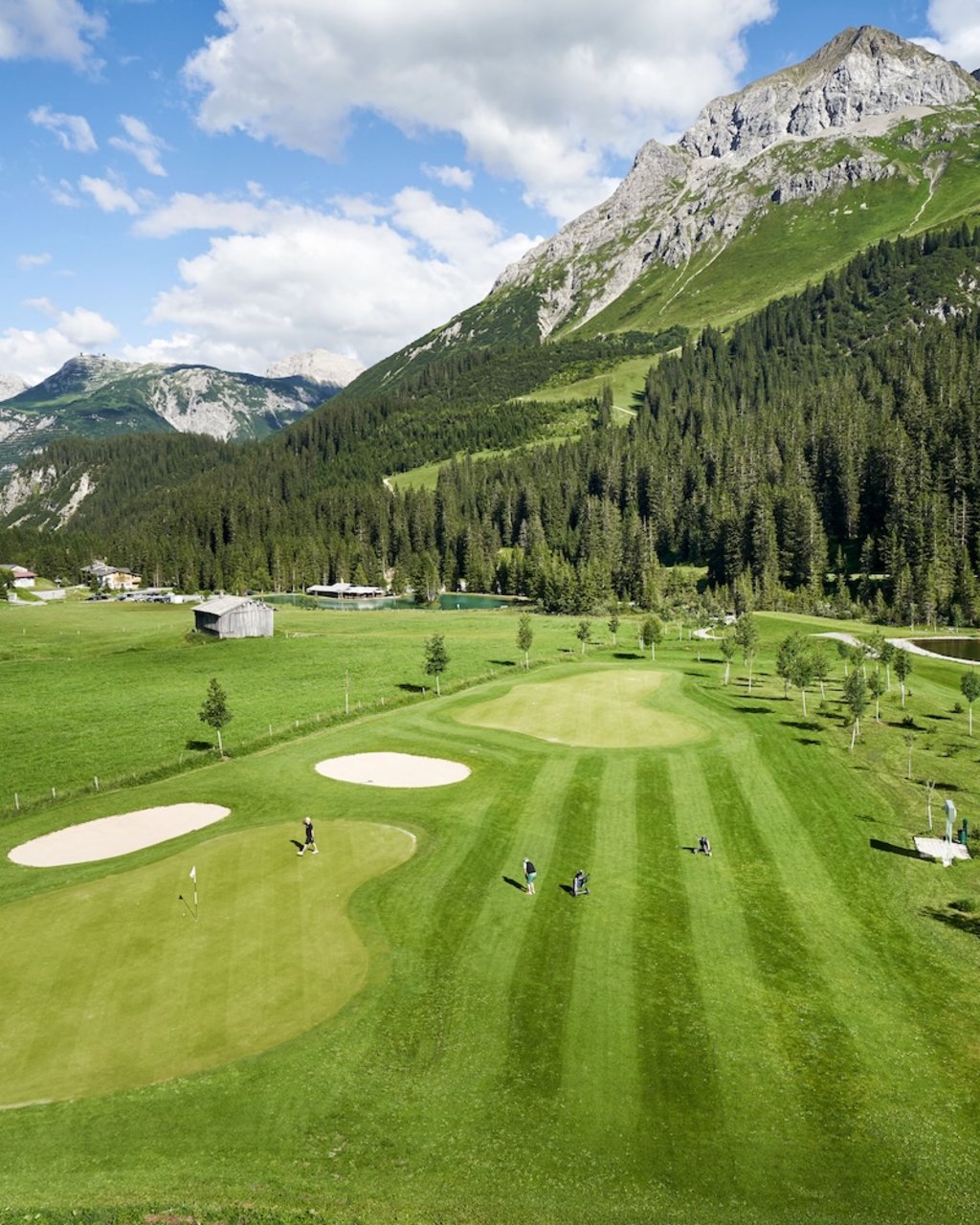 Golf players on green golf course with alpine mountains and forest landscape