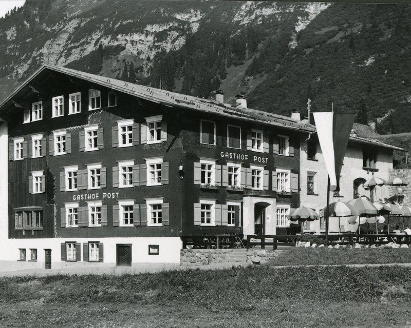 Neues aus dem Hotel Post Lech Historisches Gasthof Post mit Sonnenschirmen vor alpiner Bergkulisse