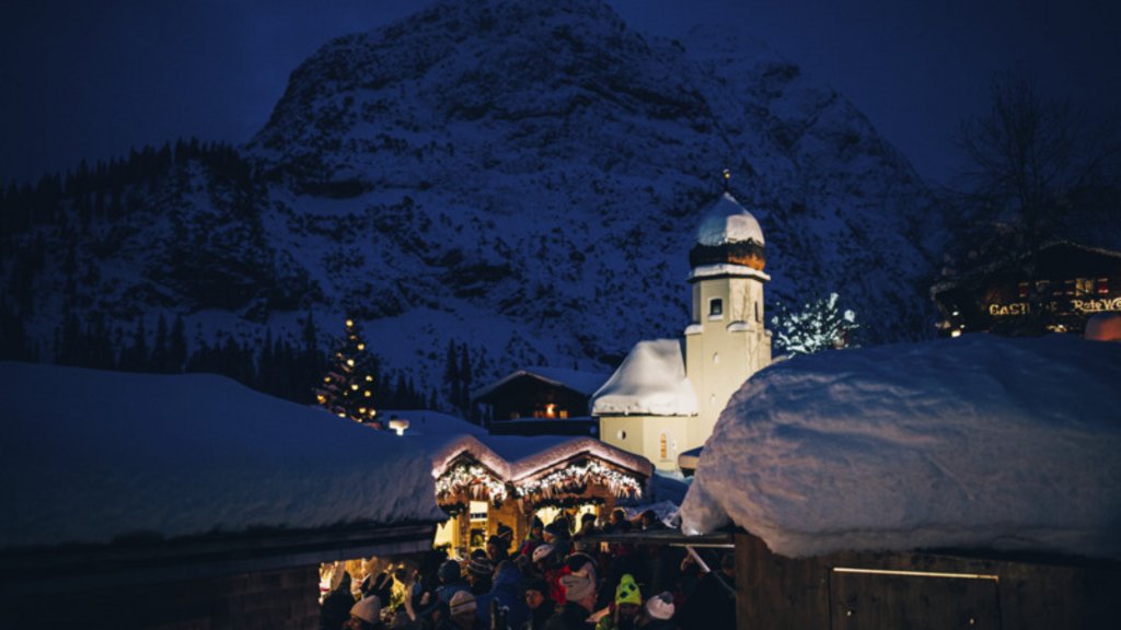 Adventzauber Winterlicher Weihnachtsmarkt bei Nacht mit schneebedeckten Hütten und Kirche vor Bergkulisse