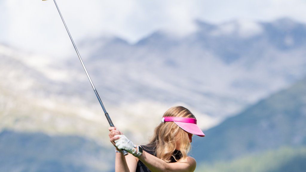 Frau mit rosa Visier beim Abschlag auf einem Golfplatz mit Bergkulisse